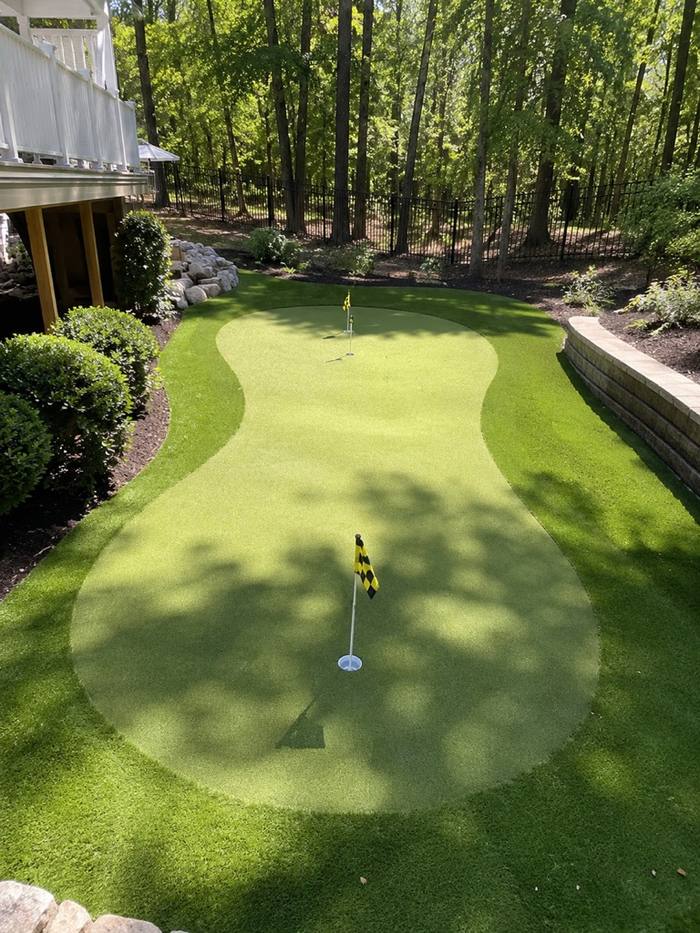 Kidney-shaped backyard putting green by pool house